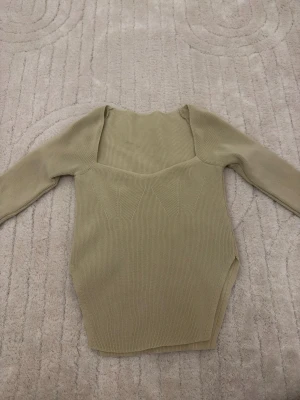 Beige ribbad långärmad topp - Säljer en beige ribbad topp med lång ärm och snyggt formad halsringning. Materialet är mjukt och stretchigt, perfekt för att skapa en clean och stilren look. Toppen har subtila detaljer framtill som ger lite extra edge.