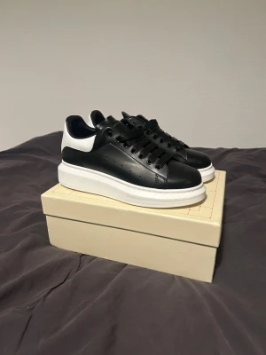 Alexander McQueen svarta sneakers - Säljer ett par svarta Alexander McQueen sneakers med vit häl och tjock vit sula. Skorna har en stilren design i läder med svarta skosnören och diskreta ventilationshål på sidorna. Aldrig använda 