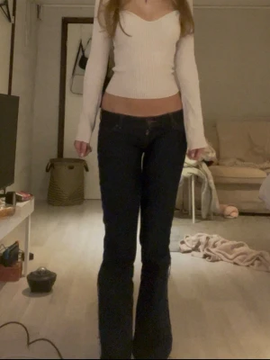 Vit ribbad croppad långärmad topp - Trendig vit croppad topp med lång ärm och v-ringad hals. Toppen är ribbad och har en figurnära passform som framhäver siluetten. Perfekt att styla med höga jeans eller kjol för en snygg look.