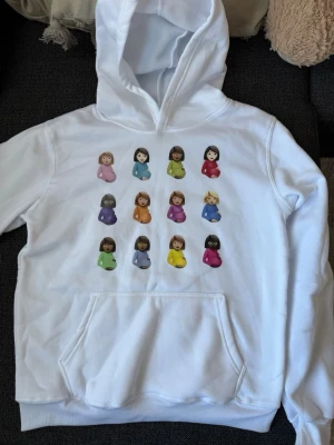 Vit Drake Certified Lover Boy hoodie - Vit hoodie med stor huva och magficka. Framsidan har tryck med emoji-motiv av gravida kvinnor i olika färger. Baksidan har samma motiv samt texten 'CERTIFIED LOVER BOY' och 'DRAKE' i svart. Materialet är mjukt och bomullsliknande.