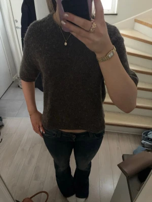 Mörkbrun stickad t-shirt - Mysig mörkbrun/grå stickad t-shirt med korta ärmar och rund hals. Tröjan har en avslappnad passform och är perfekt att styla med jeans eller kjol. Materialet ser ut att vara ull eller en ullblandning för extra komfort.
