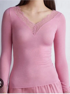 Rosa långärmad topp med spets - Supersöt rosa topp med lång ärm och v-ringning dekorerad med spetsdetaljer. Toppen har en slim passform och är perfekt för dig som gillar en feminin och stilren look. Materialet känns mjukt och stretchigt, vilket gör den bekväm att bära hela dagen.