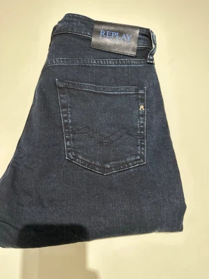 Mörkblå jeans från Replay - Snygga mörkblå jeans från Replay med klassisk femficksdesign och diskret logga på bakfickan. Jeansen har rak passform och är tillverkade i ett mjukt denimtyg som sitter bekvämt. Perfekta för en avslappnad och stilren look. Modellen är 187 och väger 70kg. Vid funderingar är det bara att skriva!