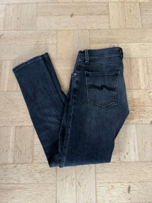 Svart/gråa Nudie Jeans  - Säljer ett par svarta/gråa Nudie Jeans med modellen Tight Terry. Dem har klassisk femficksmodell med stilrent  vågmönster på bakfickan. Jeansen har en smal passform och är tillverkade i mjuk denim med lätt tvättade detaljer.  Perfekta för en avslappnad och stilren look. Nypris cirka 1600kr säljer dem för endast 299kr Det är bara att hojta till om ni har några frågor!