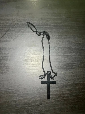 Svart halsband med korshänge - Snyggt svart halsband med ett stilrent korshänge i metall. Kedjan är tunn och enkel, vilket ger ett minimalistiskt intryck. Perfekt för dig som gillar en edgy och modern stil.