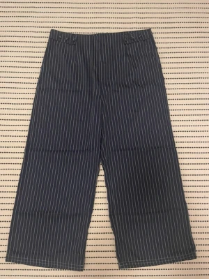 Kritstrecksrandiga kostymbyxor - Marinblå, kritstrecksrandiga, vida kostymbyxor. Köpta second hand. Medelhög midja. Storlek 42. Uppsydda så de passar mig som är 160cm perfekt i längden.  Kom gärna med bud!✨ 