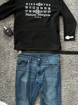 Maison Margiela  - Svart hoodie från Maison Margiela med ikoniskt tryck av siffror och logga på bröstet. Tröjan har lång ärm och klassisk huva. Tillverkad i mjukt bomullsmaterial som känns skönt mot huden. Perfekt för dig som gillar streetwear och vill sticka ut.