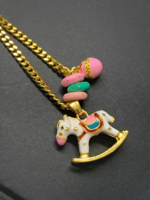 Guldhalsband med gunghäst och pärlor - Unikt halsband med guldfärgad kedja och hänge i form av en vit gunghäst med detaljer i rosa, blått och guld. Flera färgglada pärlor i rosa och turkos ger en lekfull touch. Perfekt för dig som gillar söta och färgstarka accessoarer.
