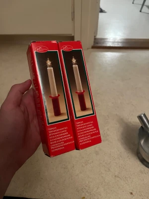 Två elektriska lucialjus i ask - Säljer två elektriska lucialjus i originalförpackning. Ljusstakarna är vita med röd fot och drivs med batteri (R6, 1.5V). Perfekta till luciatåg eller dekoration. Klassisk design och smidig att använda när levande ljus inte är ett alternativ.båda för 24kr.                                Ordinarie pris:50kr 