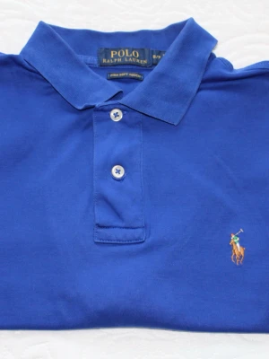 Blå pikétröja från Ralph Lauren - Klassisk blå pikétröja från Ralph Lauren med broderad logga på bröstet. Tillverkad i mjuk Pima-bomull och har krage samt knappar framtill. Perfekt för en stilren och avslappnad look.