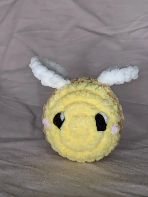 Virkat bi 🐝 - Supergulligt handvirkat bi i gult och brunt fluffigt garn med vita vingar.  Biet har svarta ögon med vita detaljer och små rosa kinder. Biet är 6 cm bred och 6 cm hög. Perfekt som dekoration eller present till någon som gillar söta saker.