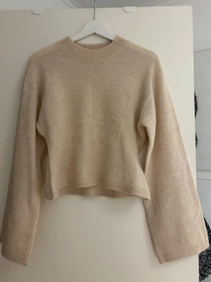 Beige stickad croppad tröja - Säljer en beige stickad tröja med croppad passform, intagen midja och långa ärmar. Tröjan har en enkel design med ribbad rund halsringning och mjukt material. Säljer då den inte kommer till användning🤍endast prövad