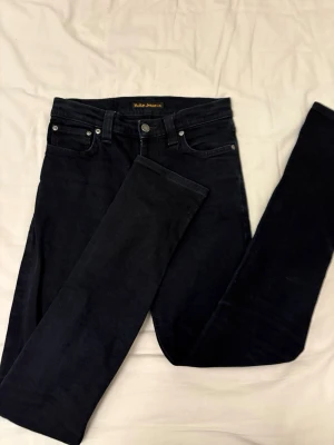 Svarta skinny jeans från Nudie Jeans - Snygga svarta skinny jeans från Nudie Jeans med klassisk femficksdesign och diskreta sömmar på bakfickorna. 