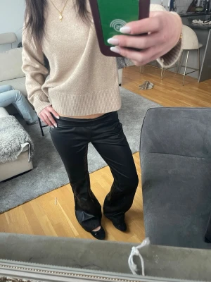 Svarta vida byxor i skinnimitation - Säljer ett par svarta byxor i skinnimitation med bootcut passform. Byxorna har en lowrise-modell och ger en cool och trendig look. Perfekta att styla med en stickad tröja eller crop top för en snygg outfit. storlek M men passar som S 