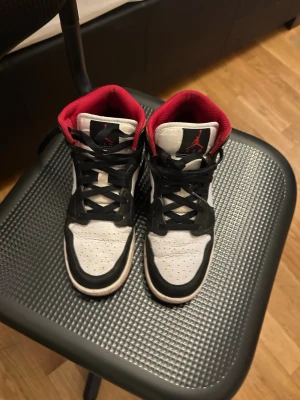 Air Jordan 1 Low svart/vit/röd - Snygga Air Jordan 1 Low sneakers i svart, vitt och rött. Skorna har svart läder på tån och snörningen, vit mesh på ovandelen och röda detaljer på swoosh, häl och insida. Klassisk Jordan-logga på plösen och vinge på hälen. Perfekta för dig som gillar streetwear.