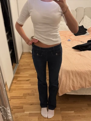 Mörkblå bootcut jeans med fickdetaljer - Säljer ett par mörkblå bootcut jeans med låg midja och snygga fickdetaljer framtill. Jeansen har klassisk femficksdesign och är tillverkade i stretchigt denimtyg för en bekväm passform. Perfekta för dig som gillar en tidlös och stilren look.