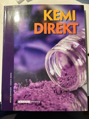 Kemi Direkt kursbok Lgr 11 - Kursboken 'Kemi Direkt' är en modern och pedagogisk lärobok i kemi, anpassad till Lgr 11. Omslaget är lila med en bild på ett glas med lila pulver. Boken har tydliga kapitel, sammanfattningar och övningar för gymnasieelever.
