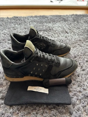 Valentino rockrunners - Snygga svarta sneakers från Valentino med coola nitar på sidorna och beige detaljer på sulan. Skorna har en klassisk låg silhuett, svarta skosnören och en ovandel i läder och mocka. Perfekta för dig som vill ha en edgy och exklusiv look.