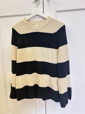Randig stickad tröja svart och beige - Säljer en stickad tröja med breda svarta och beige ränder. Tröjan har rund halsringning och långa ärmar. Ribbstickad struktur som ger en mysig och avslappnad look. Perfekt för dig som gillar klassiska färgkombinationer och enkel stil.