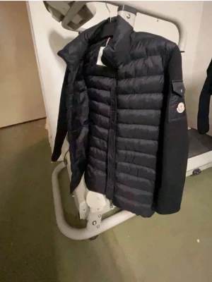 Svart pufferjacka från Moncler - Snygg svart pufferjacka från Moncler med quiltad front och släta ärmar. Jackan har hög krage, dragkedja framtill och Moncler-logga på ena ärmen. Perfekt för kalla dagar och riktigt stilren look.