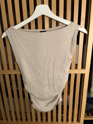 Beige ärmlös topp från Gina Tricot - Säljer en enkel och stilren beige topp från Gina Tricot. Toppen är ärmlös med bred halsringning och har en mjuk, stretchig känsla. Perfekt att matcha med jeans eller kjol för en clean look.