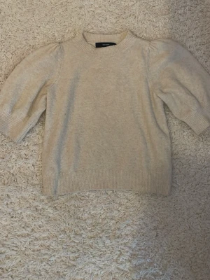 Beige stickad tröja Vero Moda - Säljer en beige stickad tröja från Vero Moda med puffärmar och ribbade muddar vid hals, ärmslut och nederkant. Tröjan har en mjuk och skön känsla, perfekt för lager på lager och enkel att matcha till olika outfits.