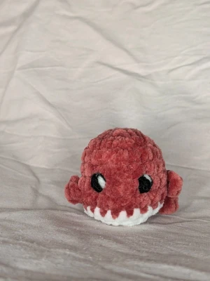 Virkad mini val 🐋 - Söt liten val plushie i röd plysch med vita detaljer och stora svarta ögon. Den är rund i formen och har små armar på sidorna. Den är 7 cm bred och 6 cm hög. Perfekt som dekoration eller mysig maskot till skrivbordet.