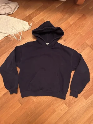 Mörkblå hoodie med huva - En enkel och stilren mörkblå hoodie med stor känguruficka framtill och klassisk huva från GinaTricot. Hoodien har ribbade muddar vid ärmslut och nederkant. Perfekt för en avslappnad och casual look. Materialet känns mjukt och bekvämt.