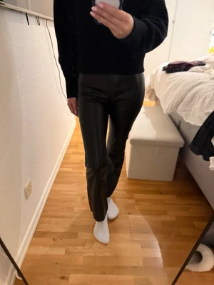 Svarta coated jeans med rak passform - Säljer ett par svarta coated jeans med rak passform och hög midja. Materialet har en glansig finish som ger en cool look. Perfekta för dig som vill ha ett par trendiga byxor som sticker ut lite extra.