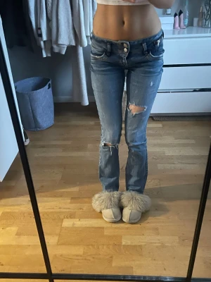 Blå slitna bootcut LTB jeans - Säljer ett par blå bootcut jeans med slitningar och hål på knäna. Jeansen har klassisk femficksdesign, låg midja och dragkedja med knapp. Perfekta för en avslappnad och trendig look. Materialet är denim i bomull.             STORLEK 27x32. Hål precis vid bakfickan jätte små inget man tänker på kan skicka bild