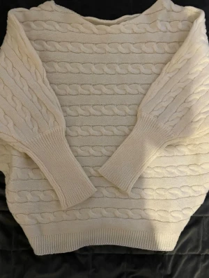 Beige stickad tröja - Stickad tröja i mjuk beige, creme färg med breda muddar vid ärmslut och nederkant. Tröjan har ett klassiskt flätmönster över hela plagget och en avslappnad passform. Toppen för dig som letar efter en vardags stil till skola eller jobb. Går att matcha med kostymbyxor, jeans mm. 