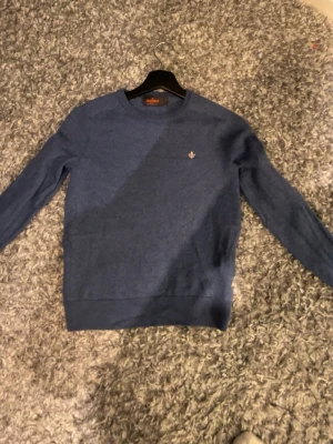 Blå stickad tröja från Morris - Snygg blå stickad tröja från Morris i 100% merinoull. Tröjan har rund halsringning, långa ärmar och en liten broderad logga på bröstet. Perfekt för dig som gillar klassisk och stilren design.