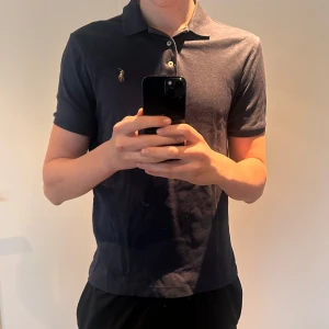 Mörkblå pikétröja från Ralph Lauren - Snygg mörkblå pikétröja från Ralph Lauren med klassisk krage och knappar. Den har en broderad logga på bröstet och korta ärmar. Toppen skick. Modellen är cirka 185cm! (Inte mina bilder)