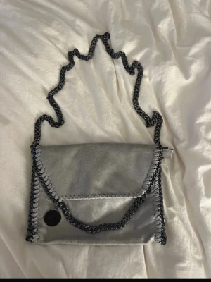 Grå axelväska med kedjerem - Snygg grå axelväska med kedjerem och dekorativa sömmar längs kanterna. Insidan är fodrad med leopardmönster. Perfekt för dig som vill ha en trendig och stilren accessoar. Vet ej vart den är ifrån, aldrig använd! (Pris kan alltid diskuteras)🩷