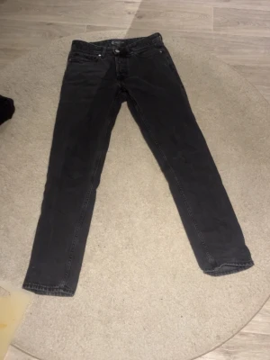 Svarta regular jeans från Cheap Monday - Säljer ett par svarta jeans från Cheap Monday i modellen Regular Rigid. Klassisk femficksdesign, raka ben och knappgylf. Jeansen är tillverkade i kraftig denim och har en stilren look som passar till det mesta.