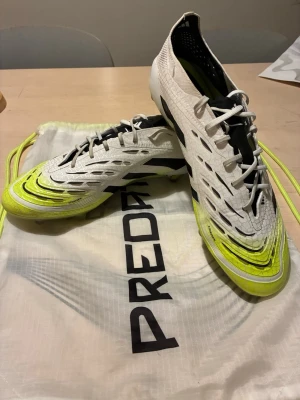 Adidas Predator fotbollsskor vit/gul - Snygga Adidas Predator fotbollsskor i vitt med neon-gula detaljer och svarta inslag. Skorna har snörning, låg profil och mönstrad ovandel för extra grepp på bollen. Levereras med tillhörande påse. Perfekta för dig som vill sticka ut på planen. De är knappt använda!