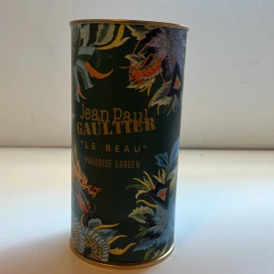 Jean Paul Gaultier Le Beau Paradise Garden - Snygg parfym från Jean Paul Gaultier, Le Beau Paradise Garden. Flaskan kommer i en cylinderformad förpackning med mörkgrön botten, guldiga detaljer och färgglada blommor och fåglar. Perfekt för dig som gillar exklusiv och unik design. Förpackningen har en buckla men gör ingen skillnad till parfym