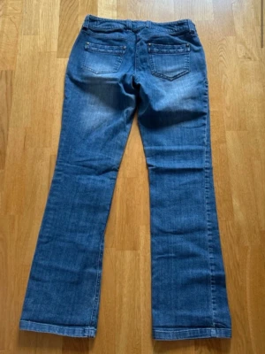 Blå bootcut  jeans - Säljer ett par blå bootcut jeans i jeansmaterial med stretchig mudd över magen. Klassisk femficksmodell och snygga slitningar framtill. Perfekta för dig som vill ha bekväma och stilrena jeans.