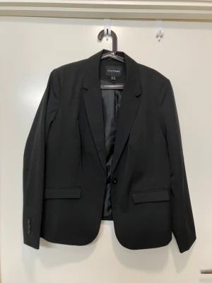 Svart kavaj från Bodyflirt - Stilren svart kavaj från Bodyflirt med klassisk passform och enkelknäppning. Kavajen har två fickor med lock framtill och slät, fodrad insida. Perfekt för en snygg och clean look. Aldrig använd. 