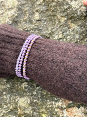 Lila pärlarmband i set om tre - Säljer ett set med tre elastiska armband gjorda av små lila och guldiga pärlor. Armbanden är tunna och kan bäras tillsammans eller separat för en personlig stil. Perfekt accessoar för att addera färg till din outfit.