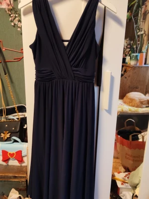 Marinblå långklänning Chiara Forthi - Elegant marinblå långklänning från Chiara Forthi med omlott överdel och breda axelband. Klänningen har v-ringning och ett mjukt, följsamt tyg som ger ett snyggt fall. Perfekt för dig som vill ha en stilren och klassisk look.