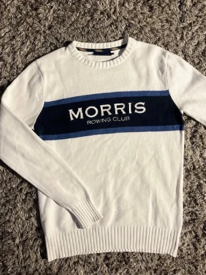 Vit stickad tröja Morris🤩🙌 - Vit stickad tröja från Morris Rowing Club med blått och svart band över bröstet och broderad logotyp. Rund halsringning och ribbade muddar vid ärmslut och nederkant. Perfekt för en sportig och stilren look.🤩🙌