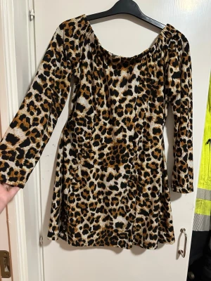Leopardmönstrad långärmad klänning storlek: M - Snygg kortklänning med leopardmönster och långa ärmar. Klänningen har en lätt utställd passform och bred urringning. Perfekt för dig som vill sticka ut med ett djurmönstrat plagg. Materialet känns mjukt och följsamt mot kroppen.