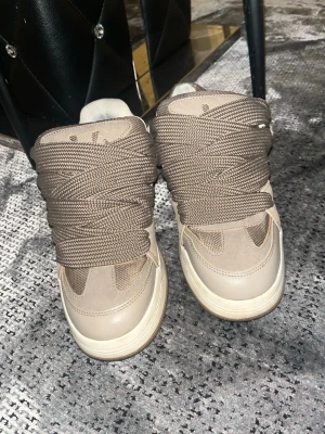 Beige chunky sneakers med breda snören - Säljer ett par beige chunky sneakers med riktigt breda snören och cool retrostil. Skorna har en mix av mocka och läderdetaljer, samt en tjock sula i gummi. Perfekta för under vintern har använts 4 gånger 