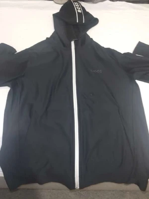 Svart hoodie med dragkedja från BOSS - Snygg svart hoodie från BOSS med vit dragkedja framtill och diskret BOSS-logga på bröstet. Huva med vit rand och BOSS-tryck på kanten. Perfekt för en avslappnad och stilren look.