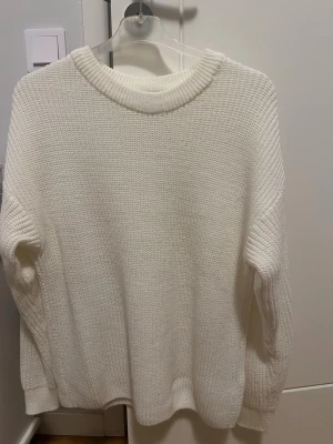 Vit stickad oversized tröja M/L - Säljer en vit stickad tröja med oversized passform och rund halsringning. Tröjan har grovstickad struktur och långa ärmar med ribbade muddar. Perfekt för lager-på-lager och enkel att matcha med olika outfits. Det enda anmärkningsbara är att den är nopprig :)