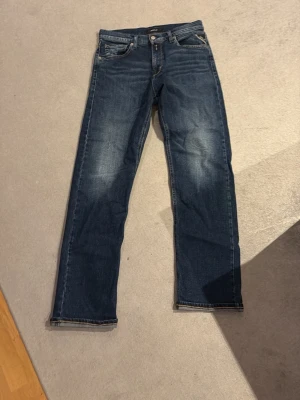 Mörkblå jeans från Replay - Snygga mörkblå jeans från Replay med klassisk femficksdesign och subtila slitningar framtill. Jeansen har raka ben och är gjorda i ett mjukt denimtyg som ger en skön passform. Perfekta för dig som vill ha en tidlös och stilren look.