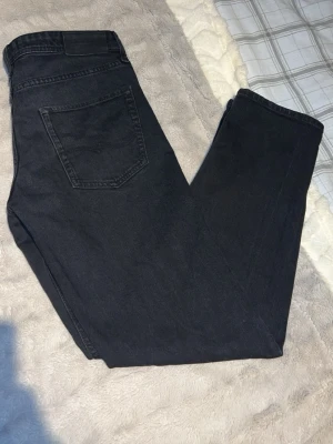 Jack & Jones jeans  - Säljer ett par svarta jeans med rak passform och klassisk femficksdesign. Jeansen har en enkel bakficka och är tillverkade i ett mjukt denimtyg. Perfekta för dig som gillar en clean och stilren look. Storlek W31 L32 