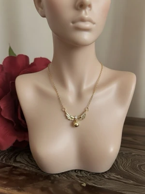 Guldigt halsband med vingar och pärldetalj - Unikt halsband i guldfärg med ett hänge format som vingar och en liten pärldetalj i mitten. Kedjan är tunn och elegant, och hänget har gnistrande stenar på vingarna för extra bling. Perfekt för dig som gillar smycken med magisk känsla.