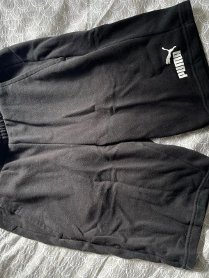 Svarta shorts från Puma - Säljer ett par svarta shorts från Puma med vit logga på vänster ben. De har elastisk midja och är gjorda i mjukt bomullsliknande material. Perfekta för träning eller chill. Klassisk och enkel design med fickor på sidorna.